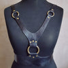 The Hel Harness, comprised of black soft genuine leather and brass rings and rivets. With a cinching wide belt and wishbone shaped straps, a leather chest harness by Hord.