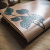Close up view of the Hop Vine Leather Journal Cover which features a hand dyed journal cover engraved with hop vines which are hand painted in green dye, by HÔRD.