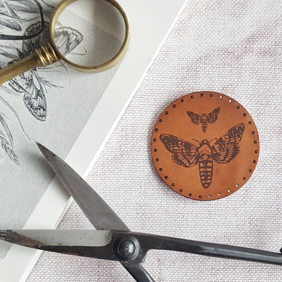 This circular leather patch is hand dyed in a medium brown and engraved with a large and small moth. Pre-cut stitch holes make it easy to sew on. The moth patch from Hord.