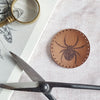 This circular leather patch is hand dyed in dark brown and engraved with a spider. This friendly little arachnid comes with stitch holes ready to easily sew onto your things. The spider patch from Hord.
