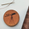 A circular leather scientist patch hand dyed in light brown dye and engraved with a vintage style telescope, perfect for men, women and children who love to gaze at the stars and beyond.