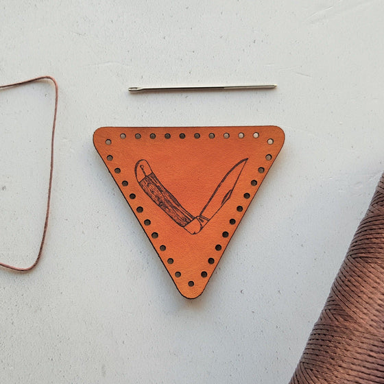 The survivalist leather patch by hord is an orange-tan trangular leather patch engraved with a partly folder Opinel style survival knife. The bushcraft patch from Hord.