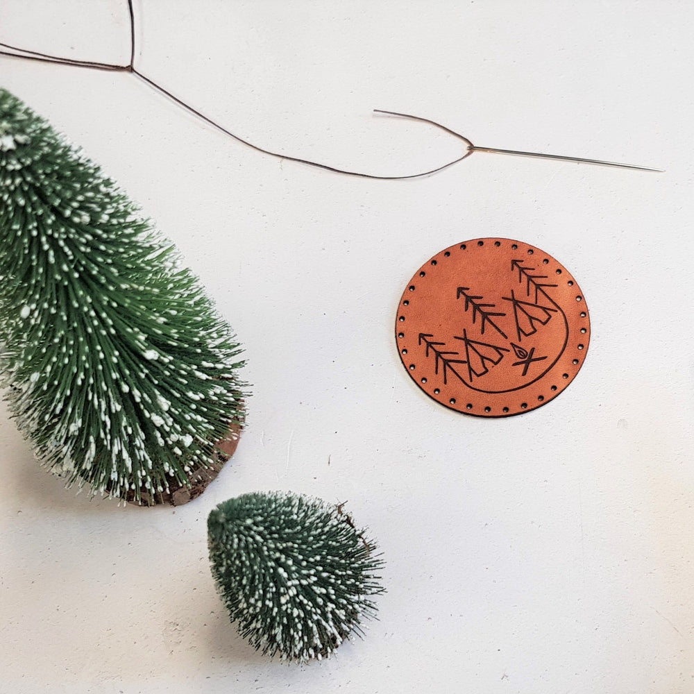 The campfire patch by HORD - a circle of light brown leather with stitch holes is emblazoned with our unique design of tents, trees and a campfire - a perfect token for people who love the outdoors