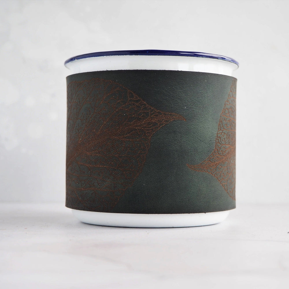 
                  
                    A camping enamel mug with a soft green leather wrap featuring a mulberry leaf engraving.
                  
                