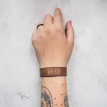  A personalised leather bracelet from Hôrd featuring a custom year. The cuff is engraved with the year 1989 in a chunky font style.