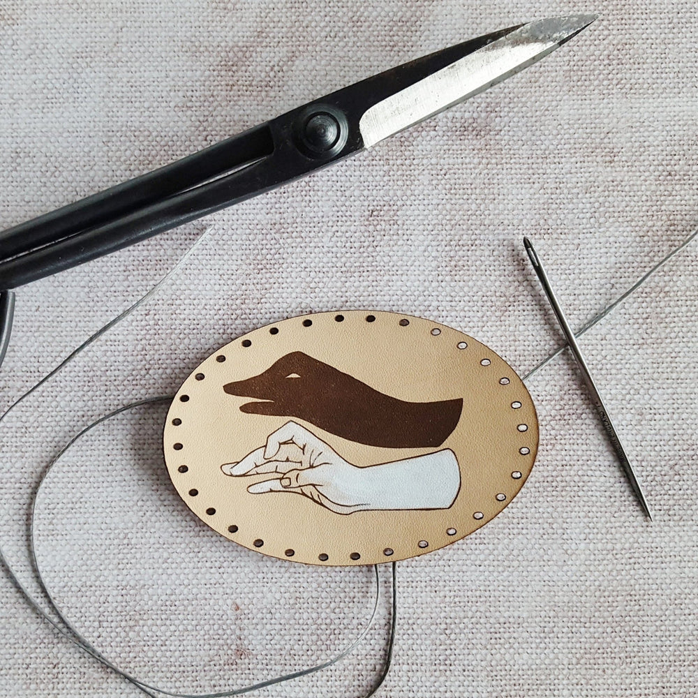 
                  
                    This natural leather goose patch is engraved and hand painted with a hand shadow puppet of a goose. 
                  
                